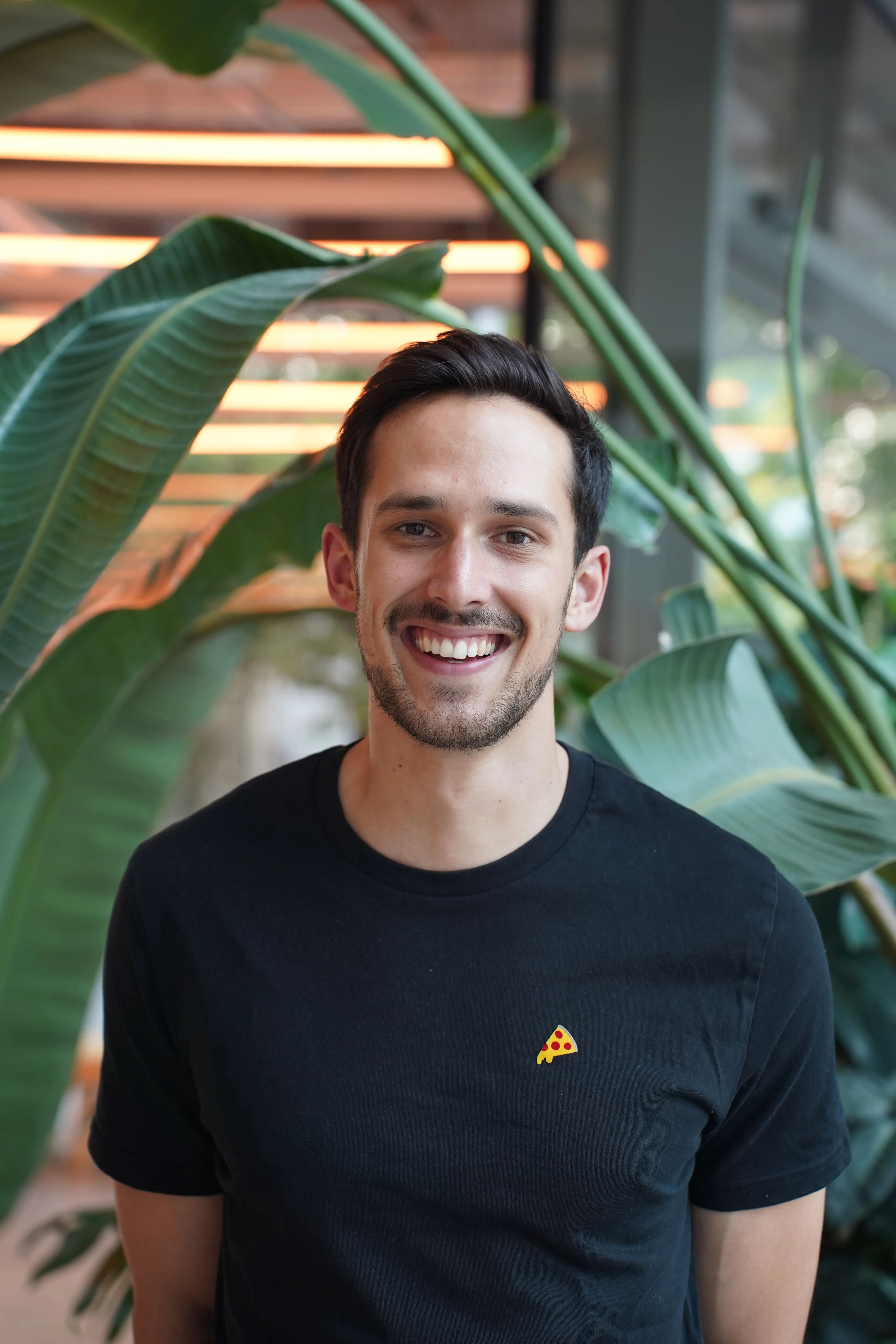 Lucas Munz, Co-founder von GIVEAJOY, lächelnd vor grünen Blättern