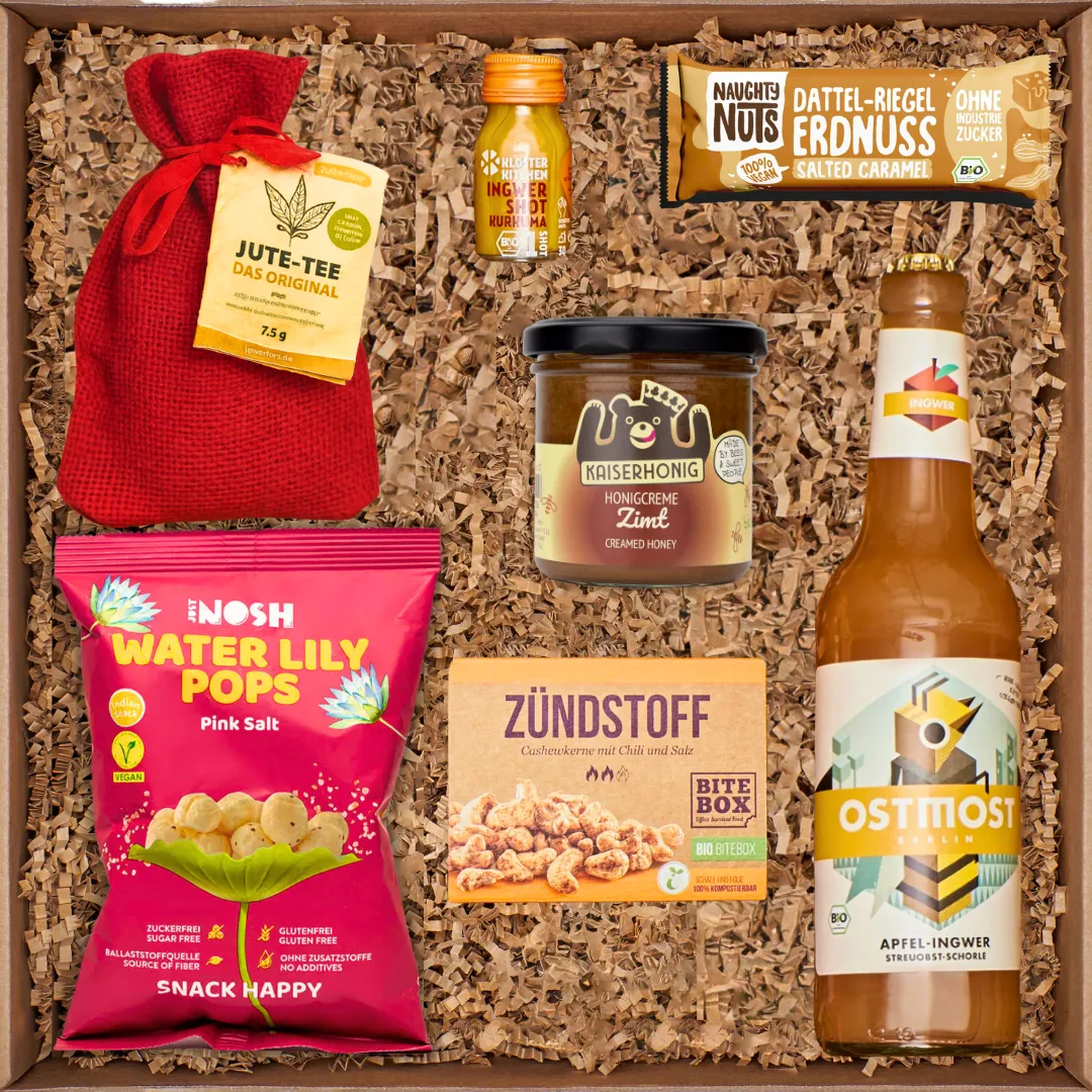 Geschenkbox mit Tee, Ingwer-Shot, Honigcreme, Erdnussriegel, Water Lily Pops, Cashew-Chili-Snack, Apfel-Ingwer-Getränk.