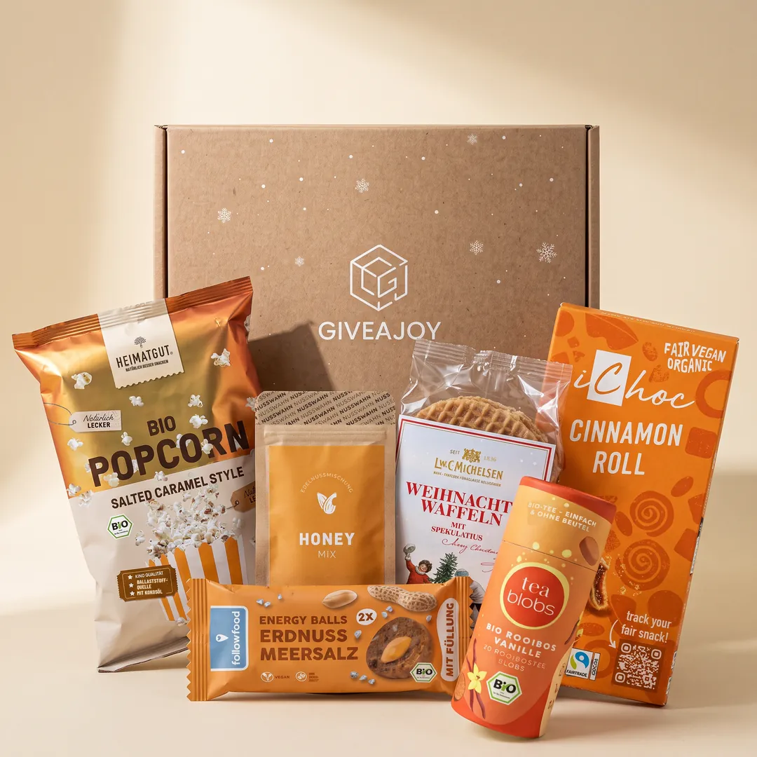 Inhalt der Weihnachtsfreude-Box vor dem GIVEAJOY-Karton: Honig-Nussmischung, Zimtschokolade, Weihnachtswaffeln, Energy Ball, Rooibos-Tee und Popcorn Salted Caramel.
