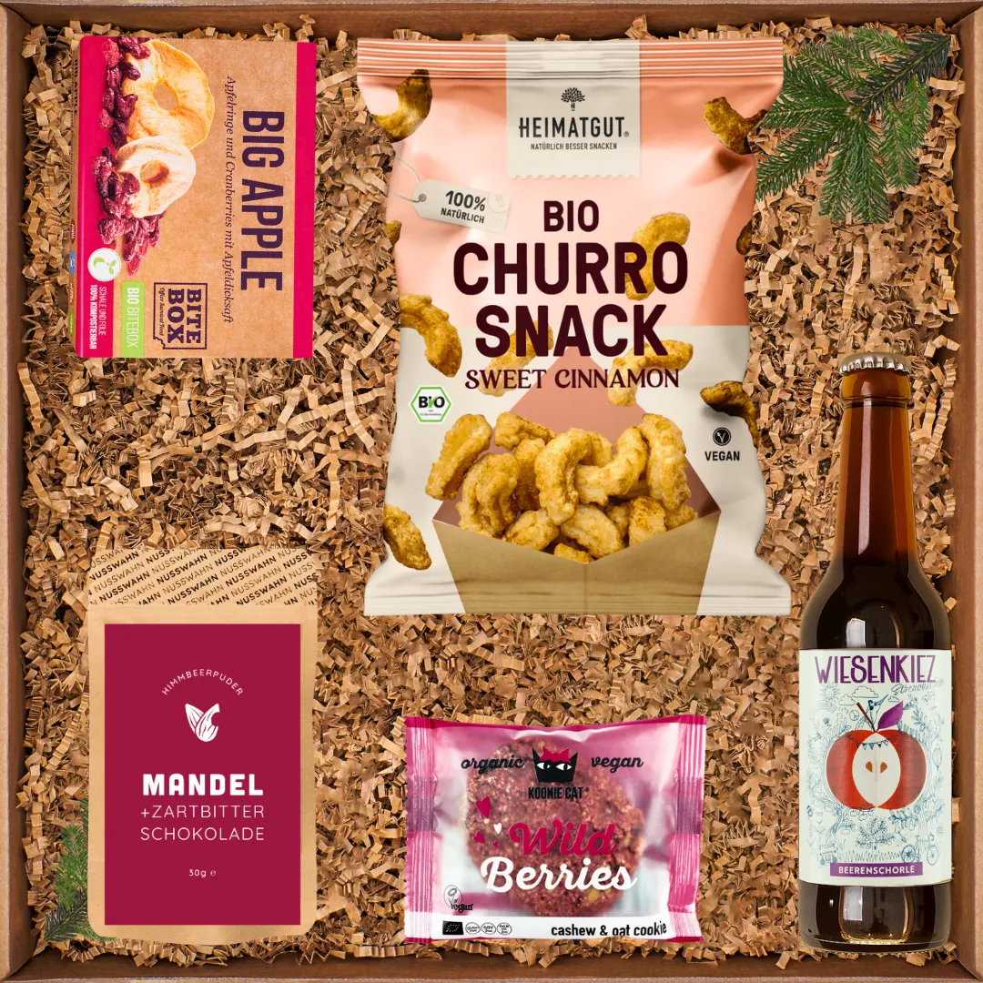 Geschenkkarton mit Bio-Snacks: Big Apple Trockenfrüchte, Bio-Churro-Snack, Mandelschokolade, Wild Berries und Beerenschorle.