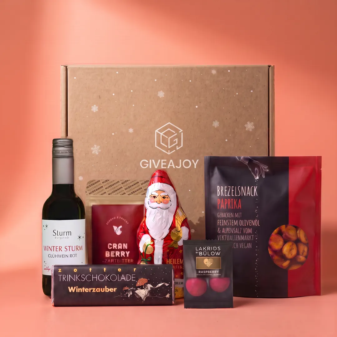 Inhalt der Weihnachtstradition-Box vor dem GIVEAJOY-Karton: Brezelsnack, Lakritz, Cranberry-Zartbitter, Glühwein Rot, Schokofigur und Trinkschokolade.
